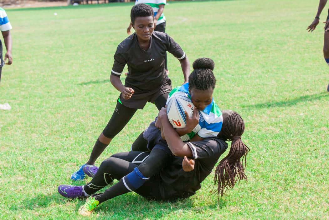 Picture shows two female rugby players in a tackle watched by a referee